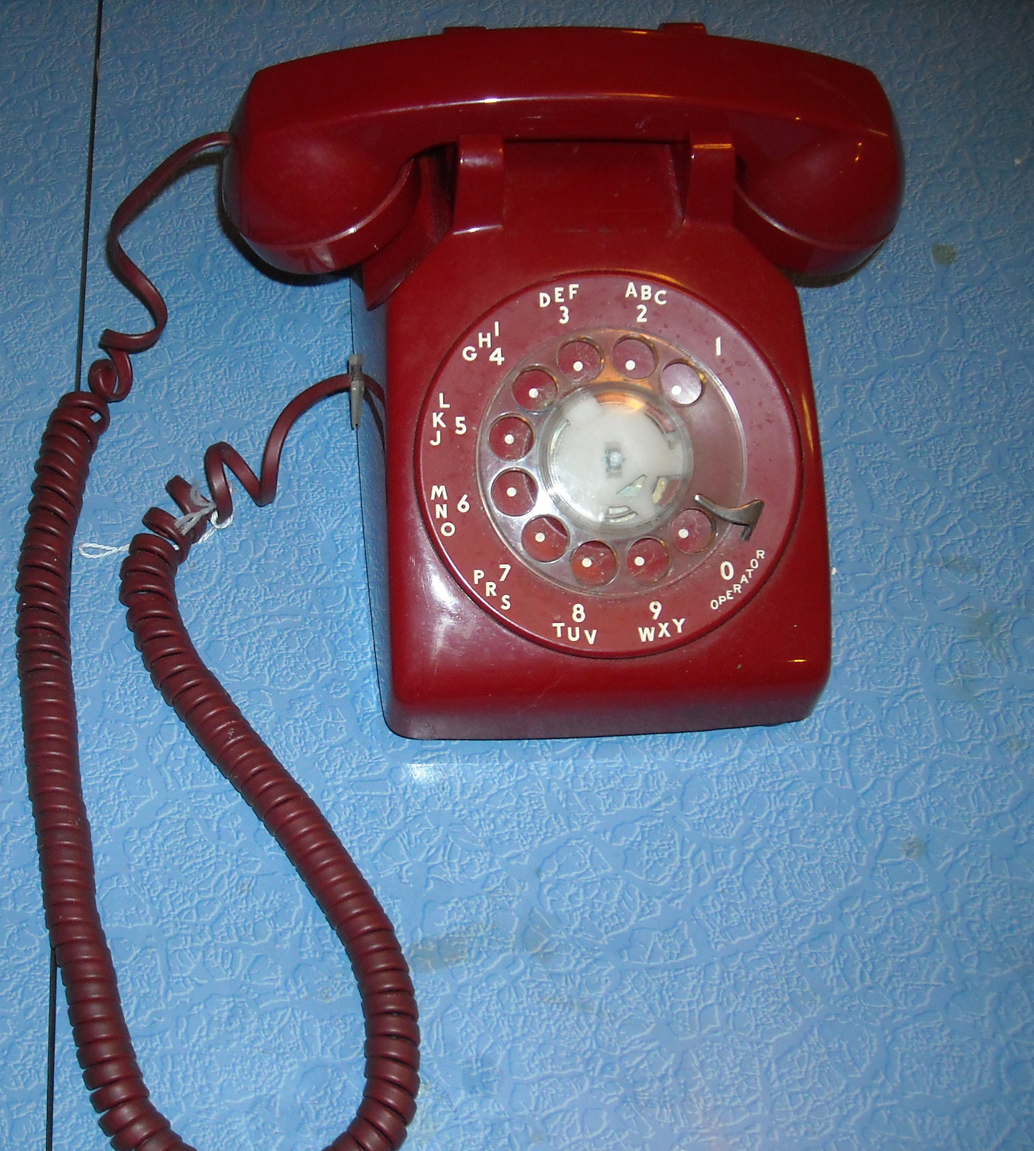 A real red rotary telephone on a blue wall